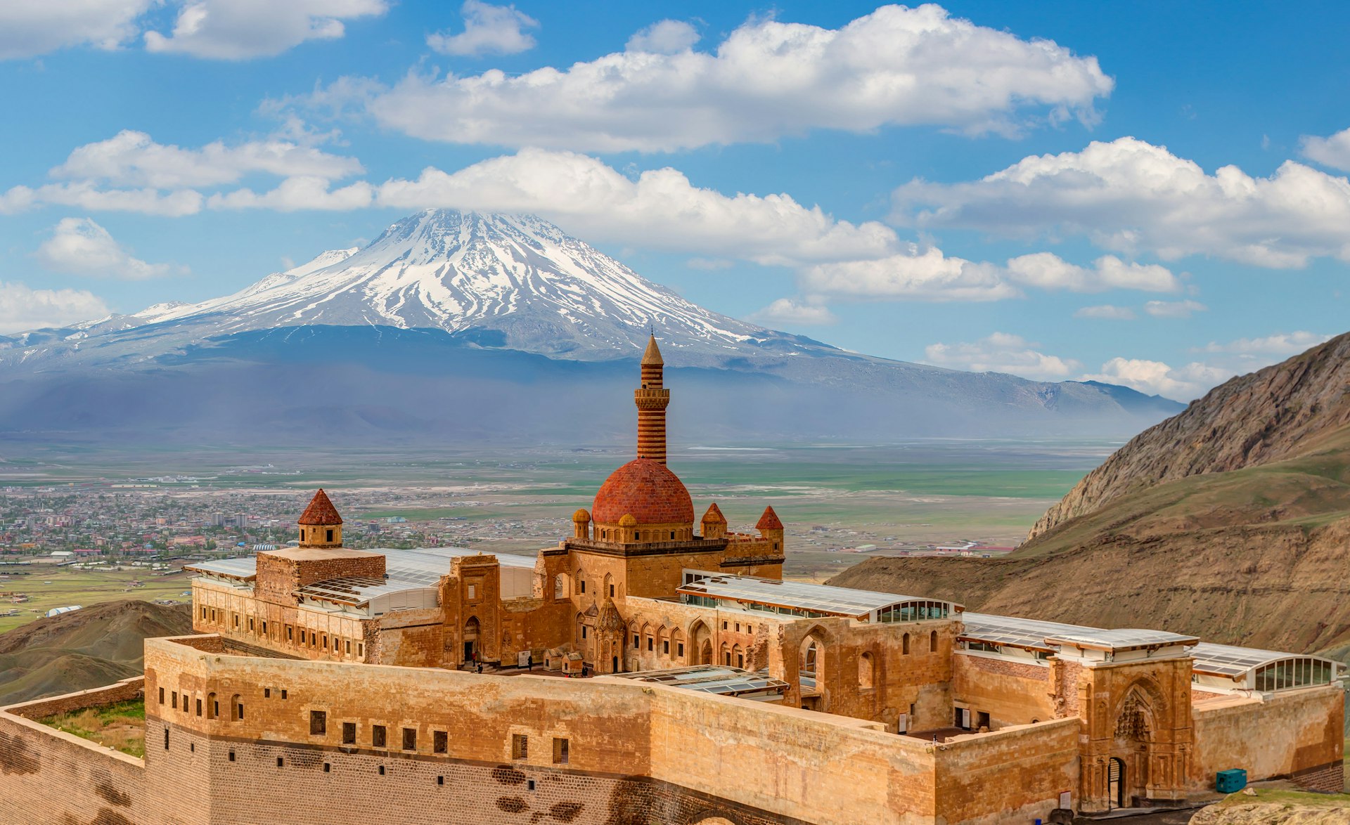 A red-stone palace with a central domed tower. A snow-capped mountain rises in the distance