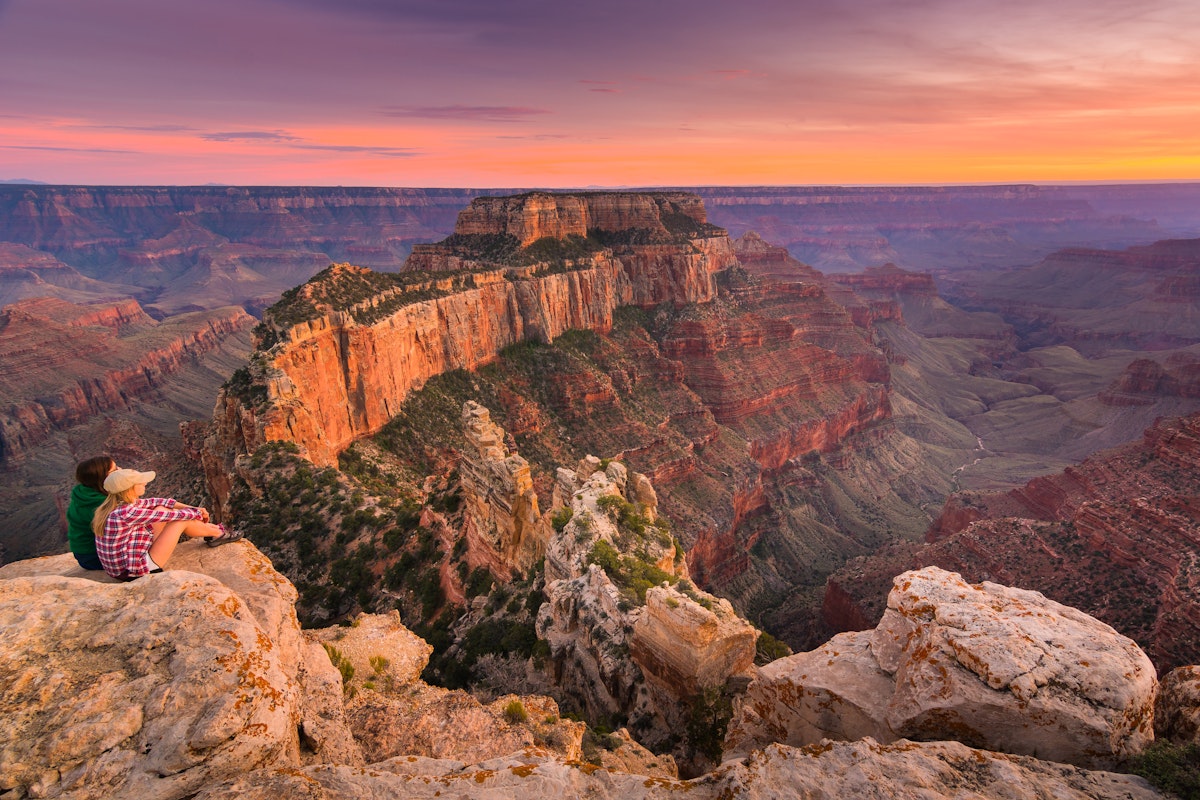 Group of people sitting near the edge watching sunset at Grand Canyon National Park North Rim, USA.