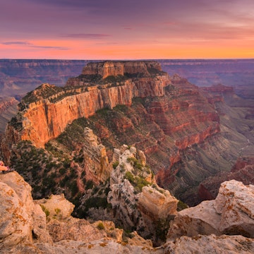 Group of people sitting near the edge watching sunset at Grand Canyon National Park North Rim, USA.