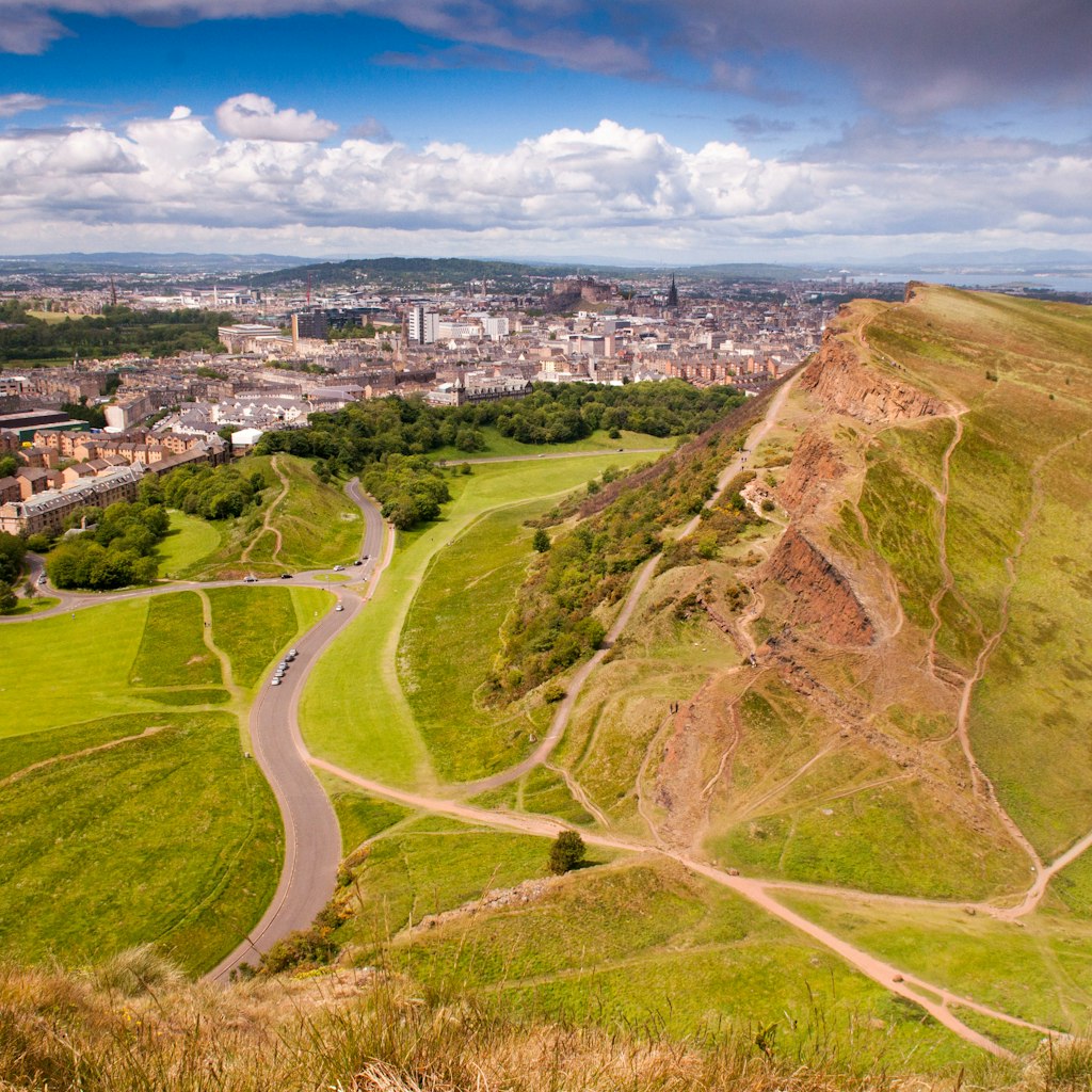 The Edinburgh cityscape, including the Old Town and Edinburgh Castle, seen from Arthur's Seat on a sunny summer's day, with Salisbury Crags and Holyrood Park in the foreground.