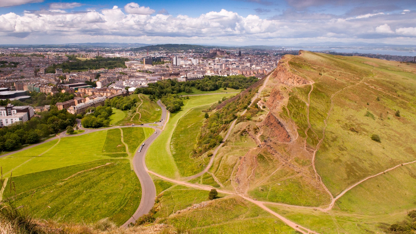 The Edinburgh cityscape, including the Old Town and Edinburgh Castle, seen from Arthur's Seat on a sunny summer's day, with Salisbury Crags and Holyrood Park in the foreground.