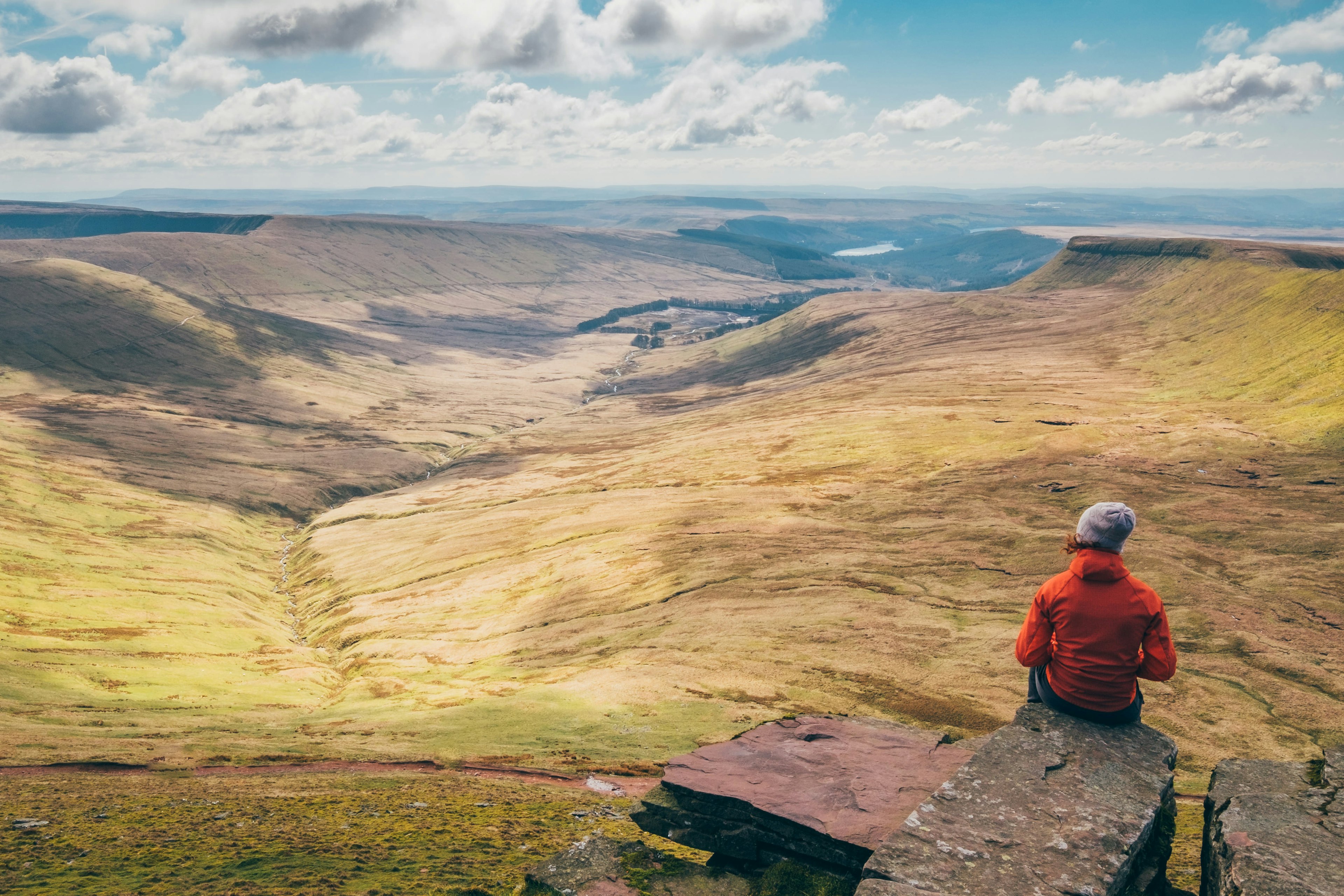 A hiker sits at a peak looking out over the rolling hills