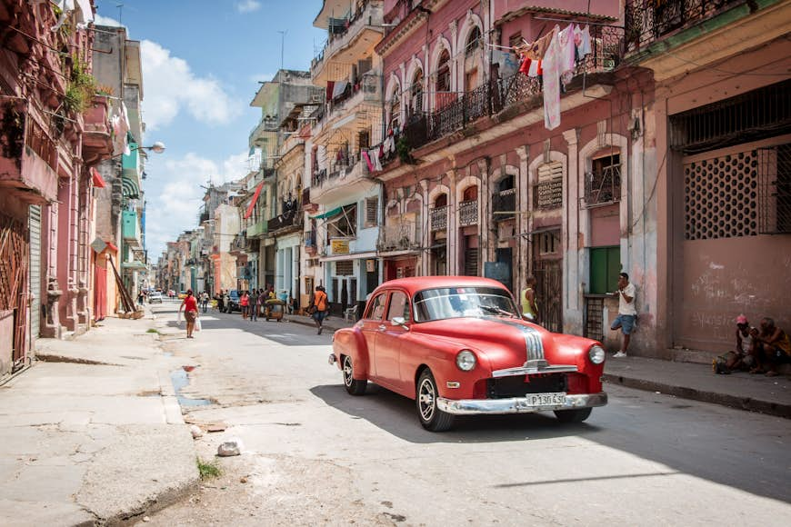 Classic red American car being used as a taxi in downtown Havana, Cuba, with locals.