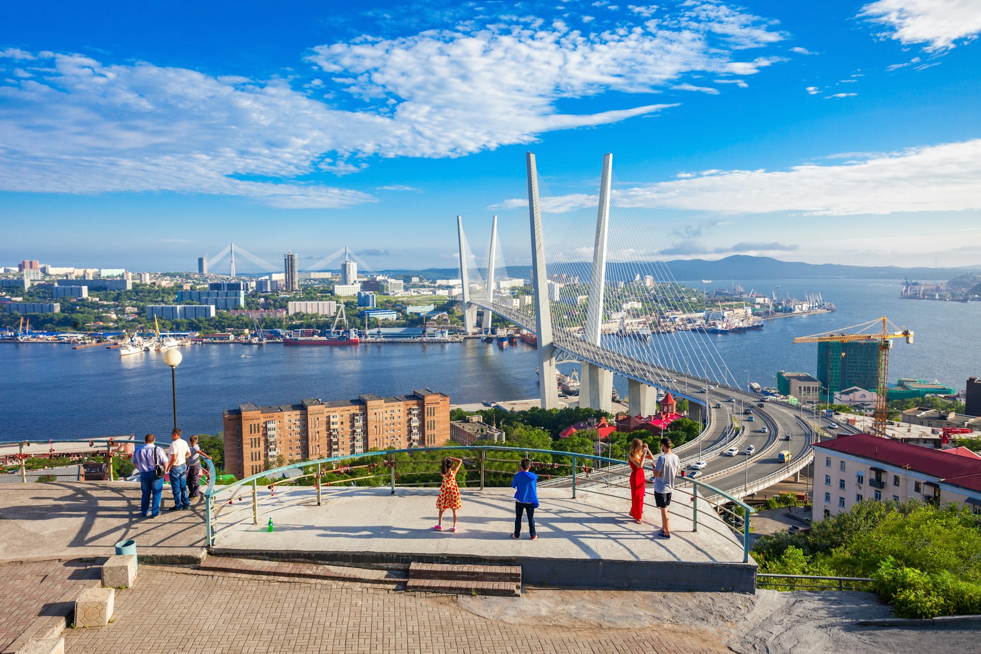 People stand at a viewpoint looking out at a huge road bridge over a body of water