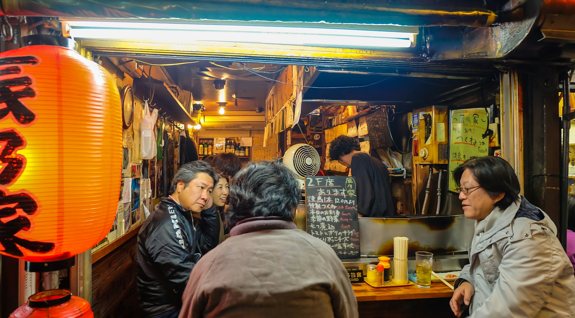 d Japanese man grills BBQ to customers in a tiny Japanese BBQ food stall at Omoide Yokocho, Shinjuku.