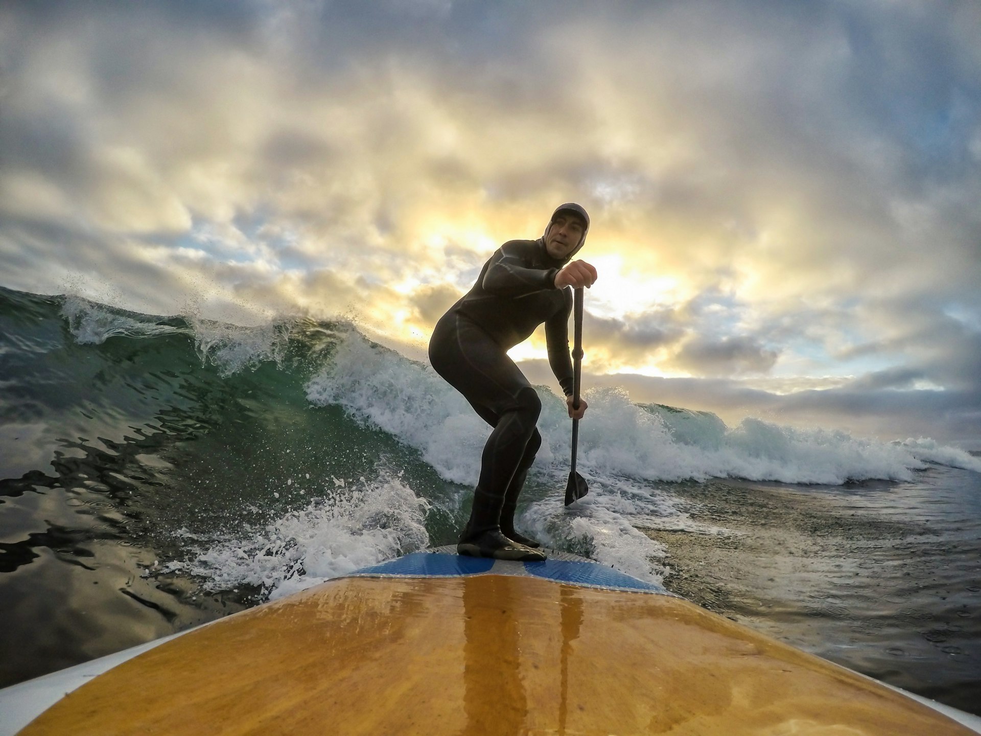 Man paddle surfing waves at the Pacific Ocean in Tofino during a cloudy winter sunset. 