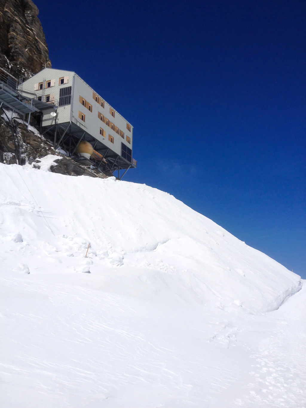 The Monchsjochhutte is a large alpine hut (more like a large house) in the Jungfrau Region of Switzerland. It half hangs over the side of a rocky platform, and is supported by struts.