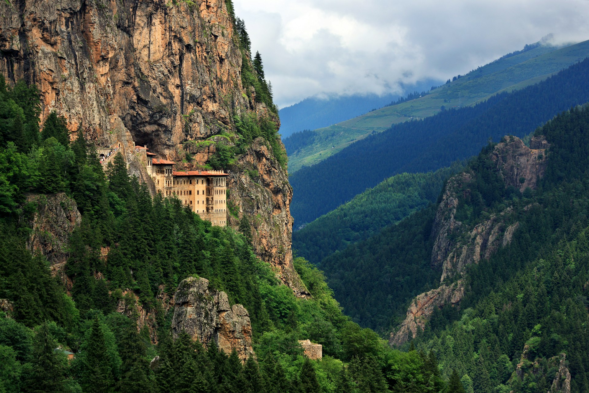 A monastery building built into the side of a huge cliff high up above a valley