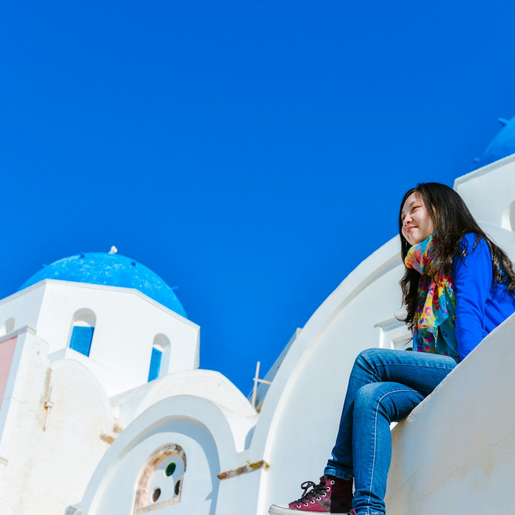 Single woman sitting on edge of roof top at Oia town, Santorini, Greece