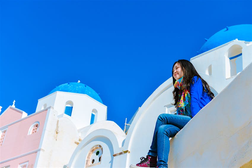 Single woman sitting on edge of roof top at Oia town, Santorini, Greece