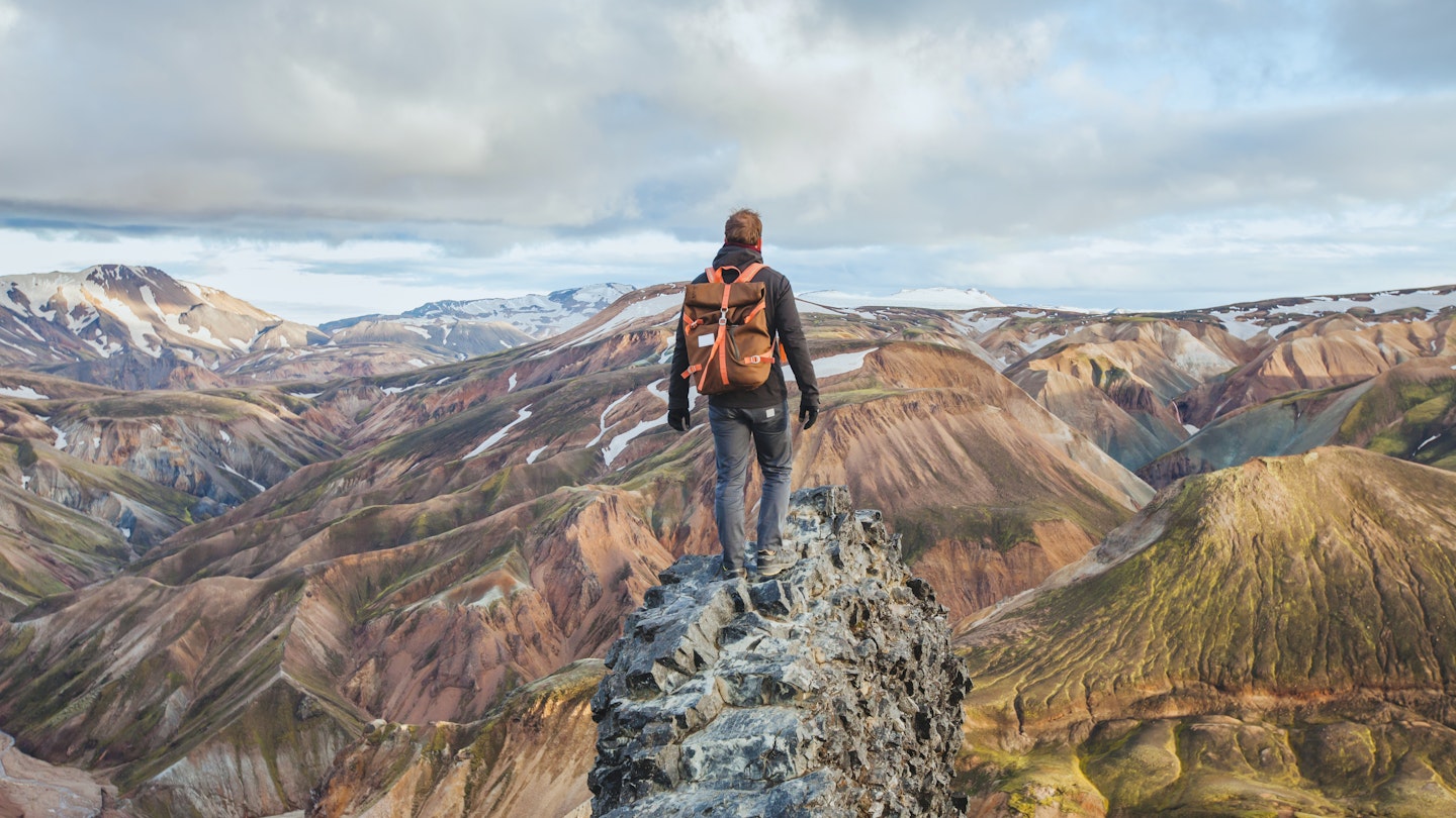 adventure travel, hiking in Iceland with a backpack, tourist looking at the colorful landscape of Landmannalaugar