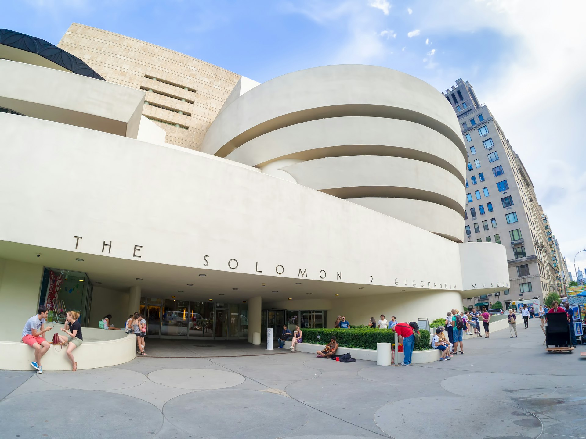 Groups of people sit on the stone ledges outside The Solomon R. Guggenheim Museum in New York City. 
