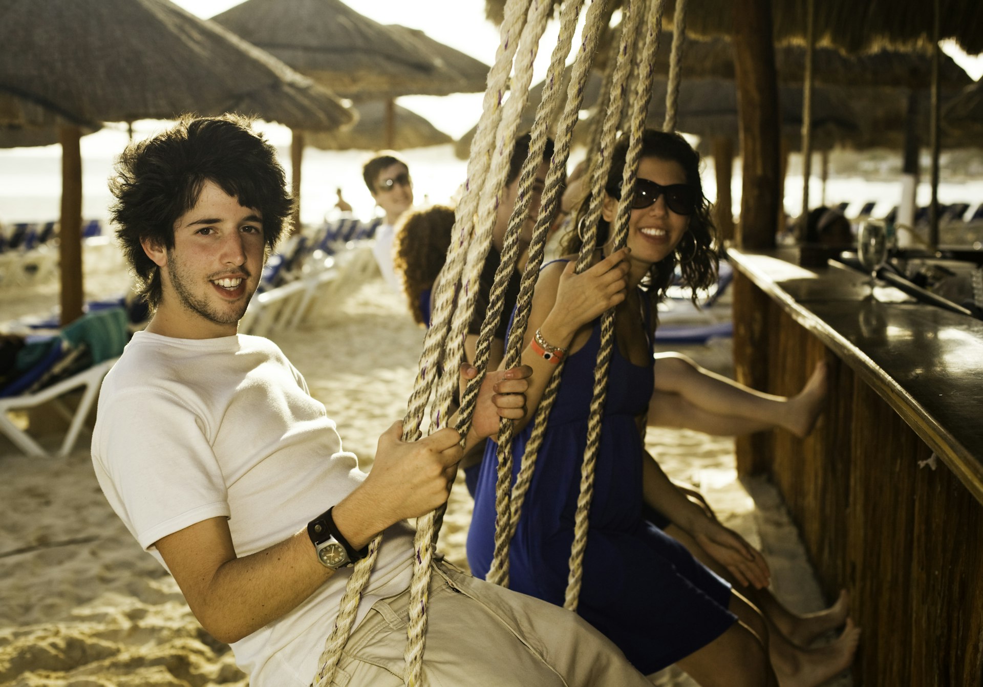 Two friends sit on swings at a beach bar