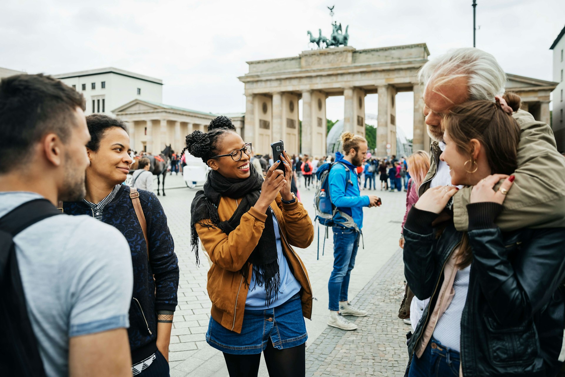 A young woman takes a photo of friends at Brandenburg Gate in Berlin, Germany