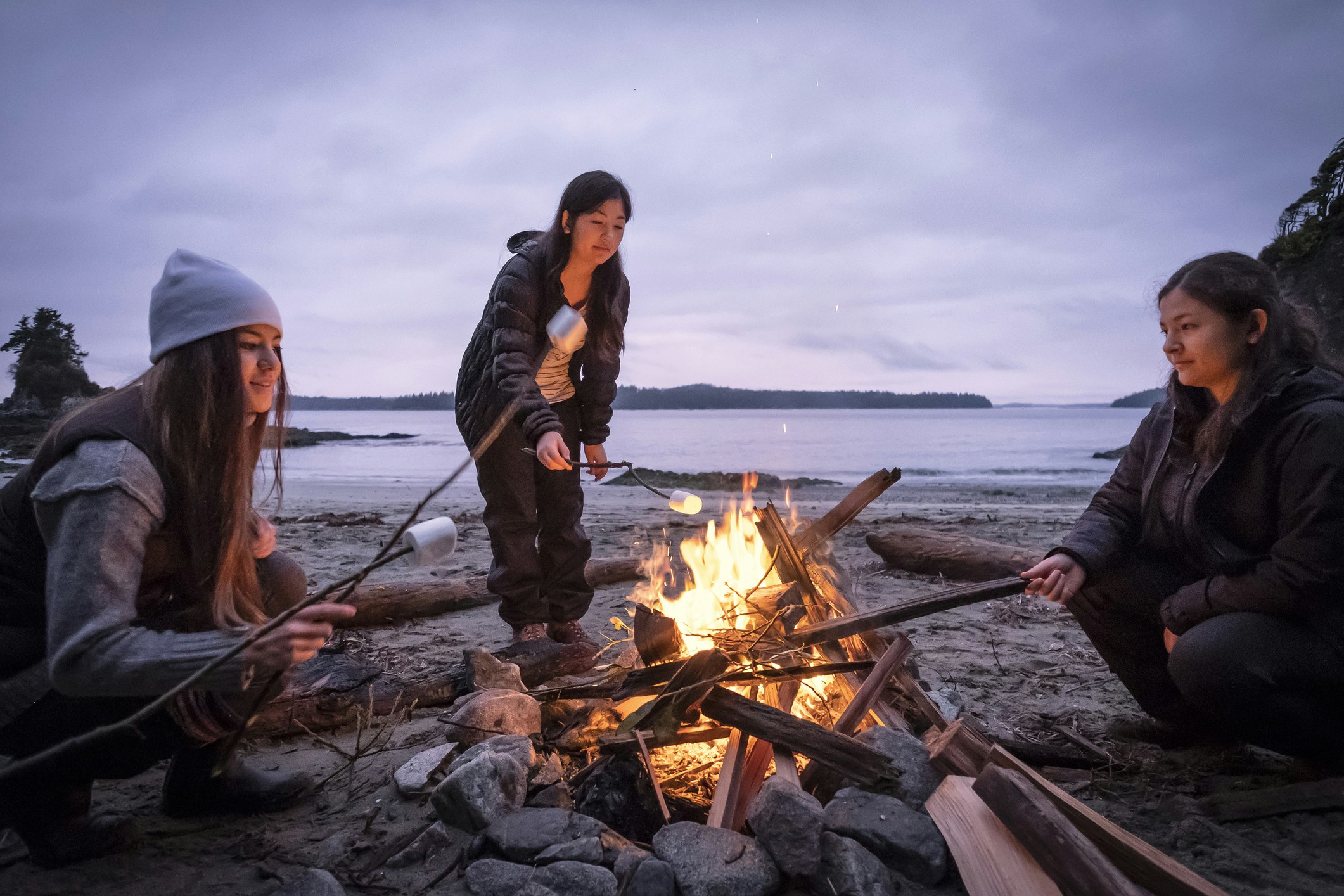 Young women roasting marshmallows on campfire on remote winter beach Tasmin Waby