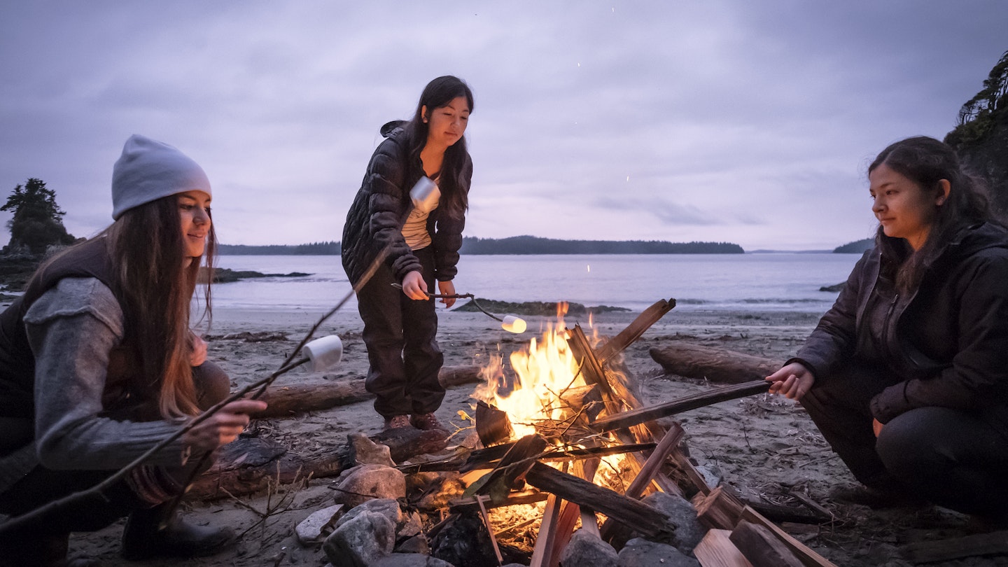 Mixed ethnic, Eurasian sisters roast marshmallows on sticks.  Bamfield, Vancouver Island, British Columbia, Canada.