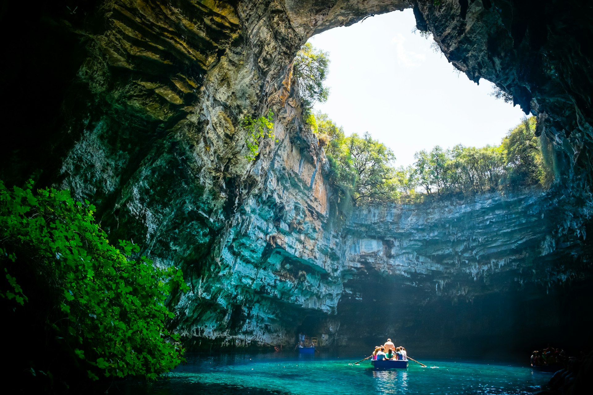 A small boat loaded with passengers in a huge cavern with bright turquoise waters below