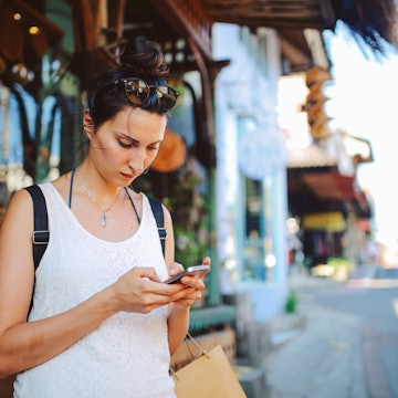 Young woman with a backpack traveling in Bali, Indonesia. She is checking her mobile phone, looking for travel tips on where to go next.