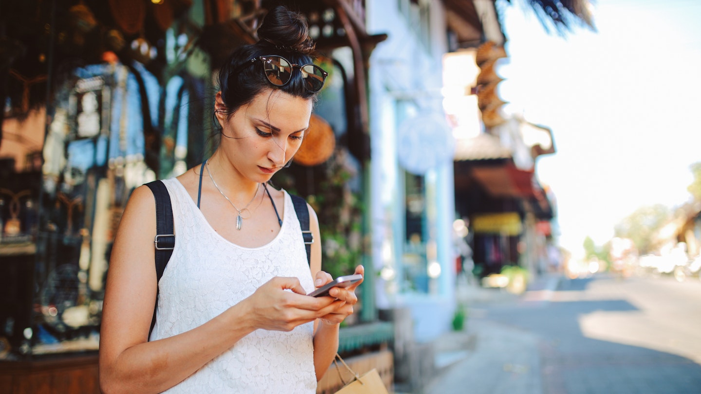Young woman with a backpack traveling in Bali, Indonesia. She is checking her mobile phone, looking for travel tips on where to go next.