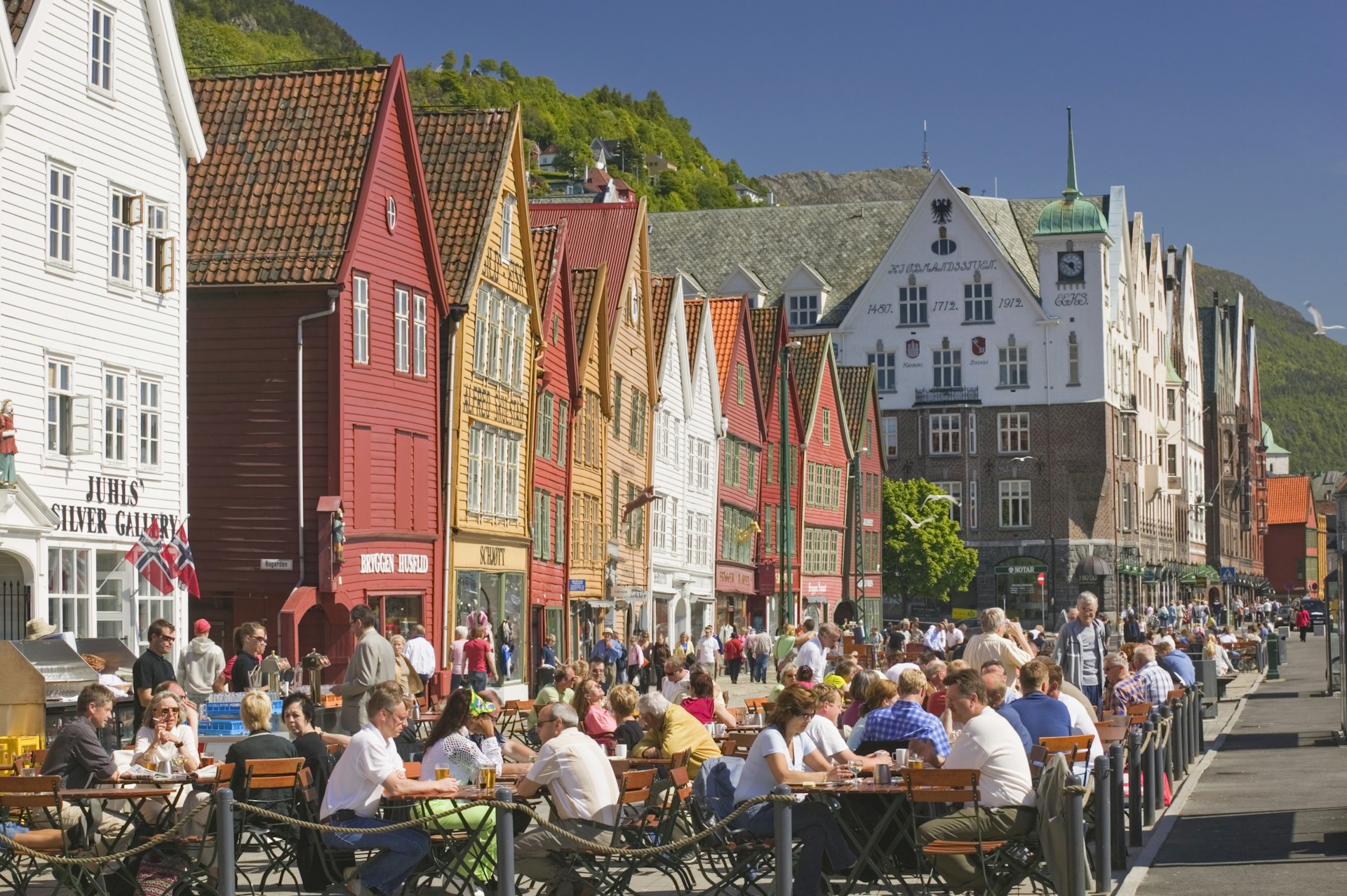 People sit at tables outside the colourful buildings of the harbourside Bryggen district in Bergen
