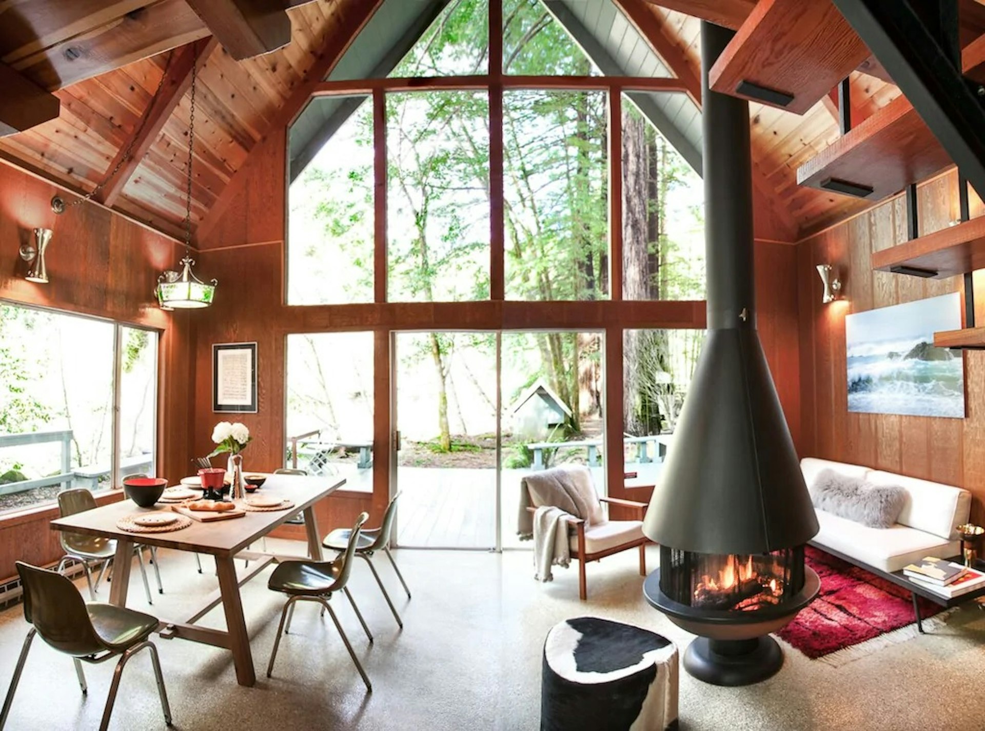 A wood-paneled cabin with a midcentury modern dining table and fireplace