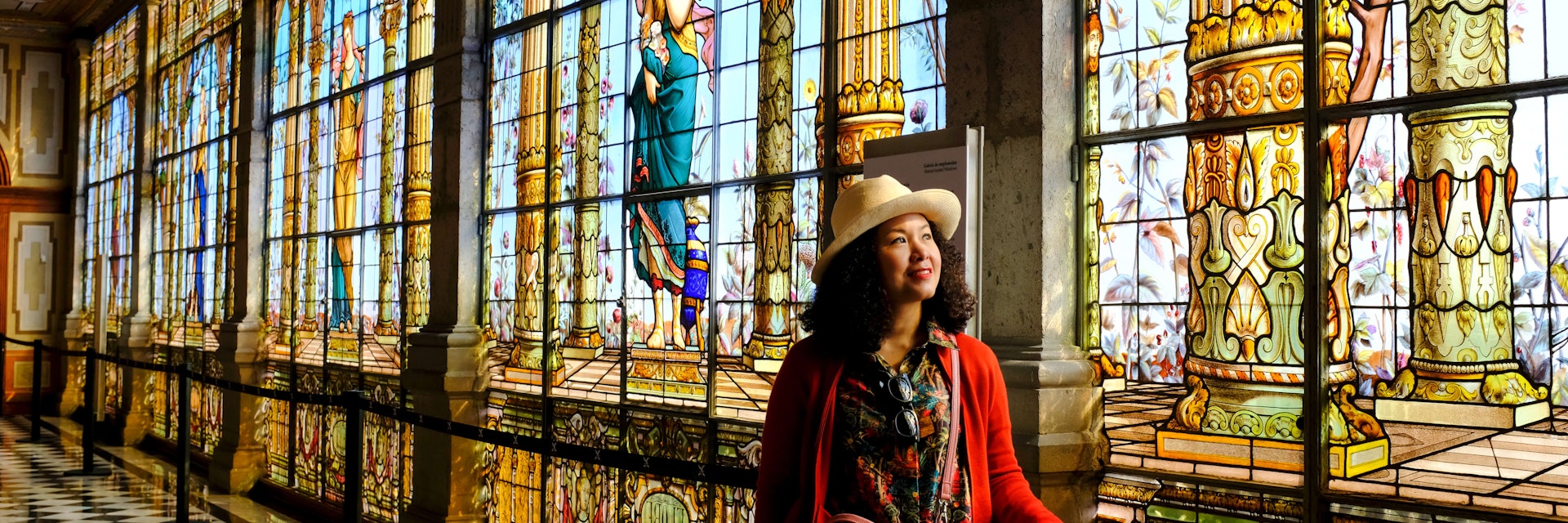 A tourist admiring the beautiful stained glass windows along a corridor inside Chapultepec Castle.