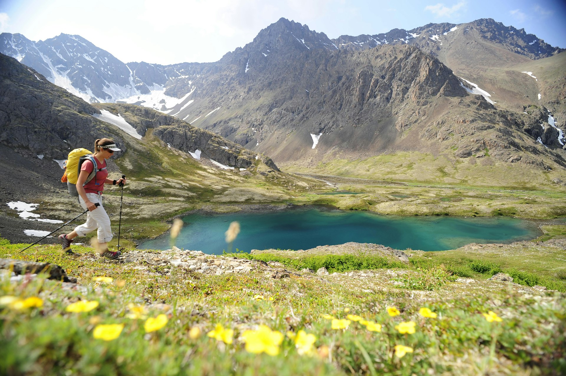 A woman hikes through a spring landscape with melting snow on the mountain behind her