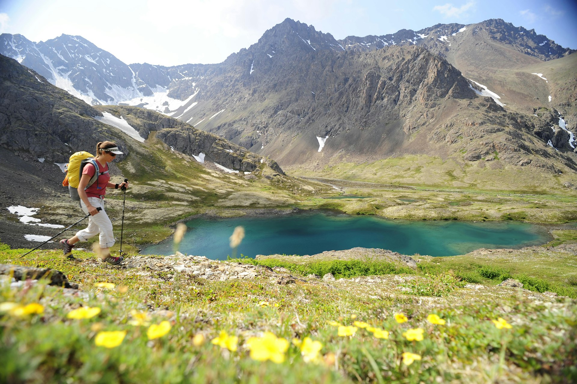 Una mujer camina por un paisaje primaveral con nieve derretida en la montaña detrás de ella