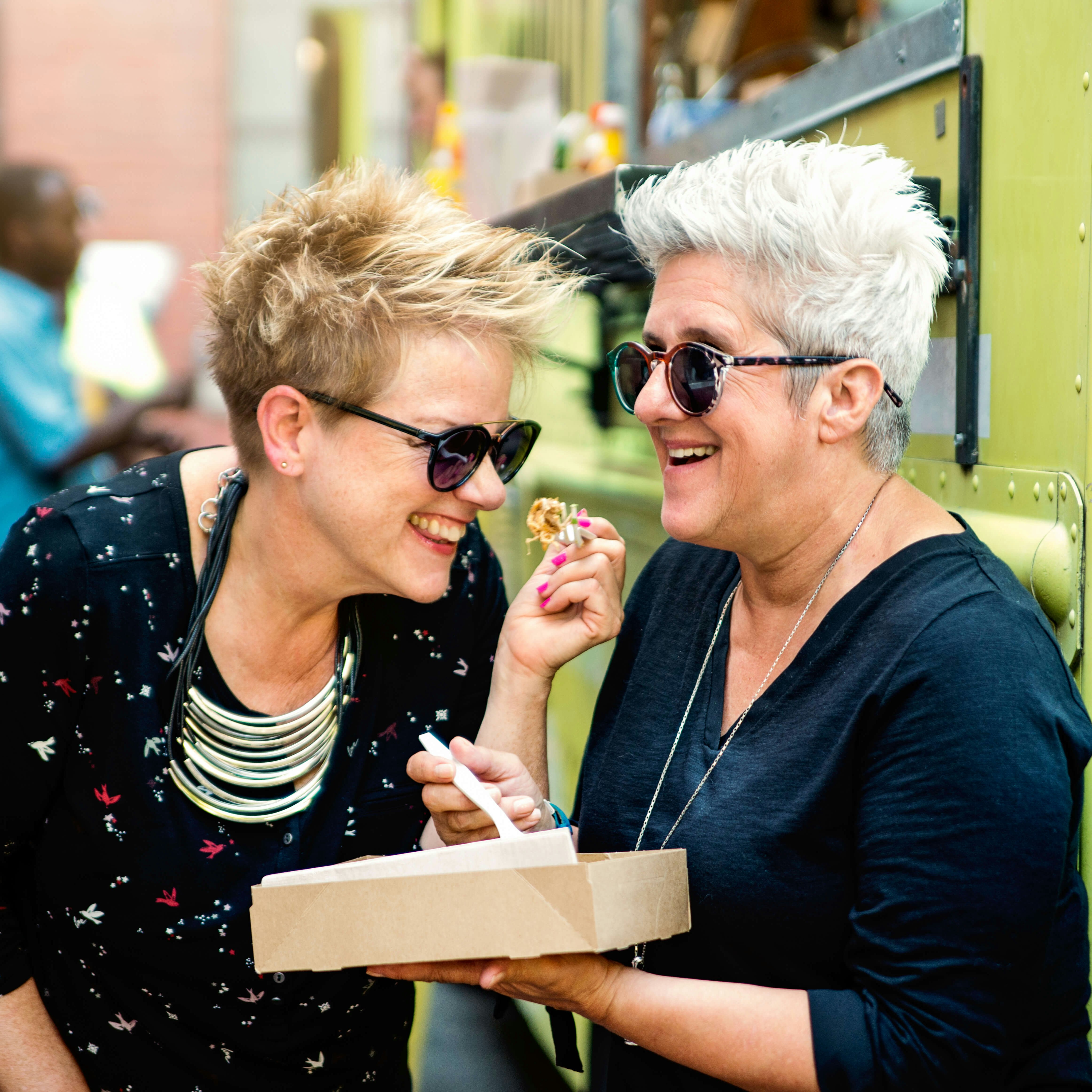 Couple of mature women enjoying their food from a food truck in city street.