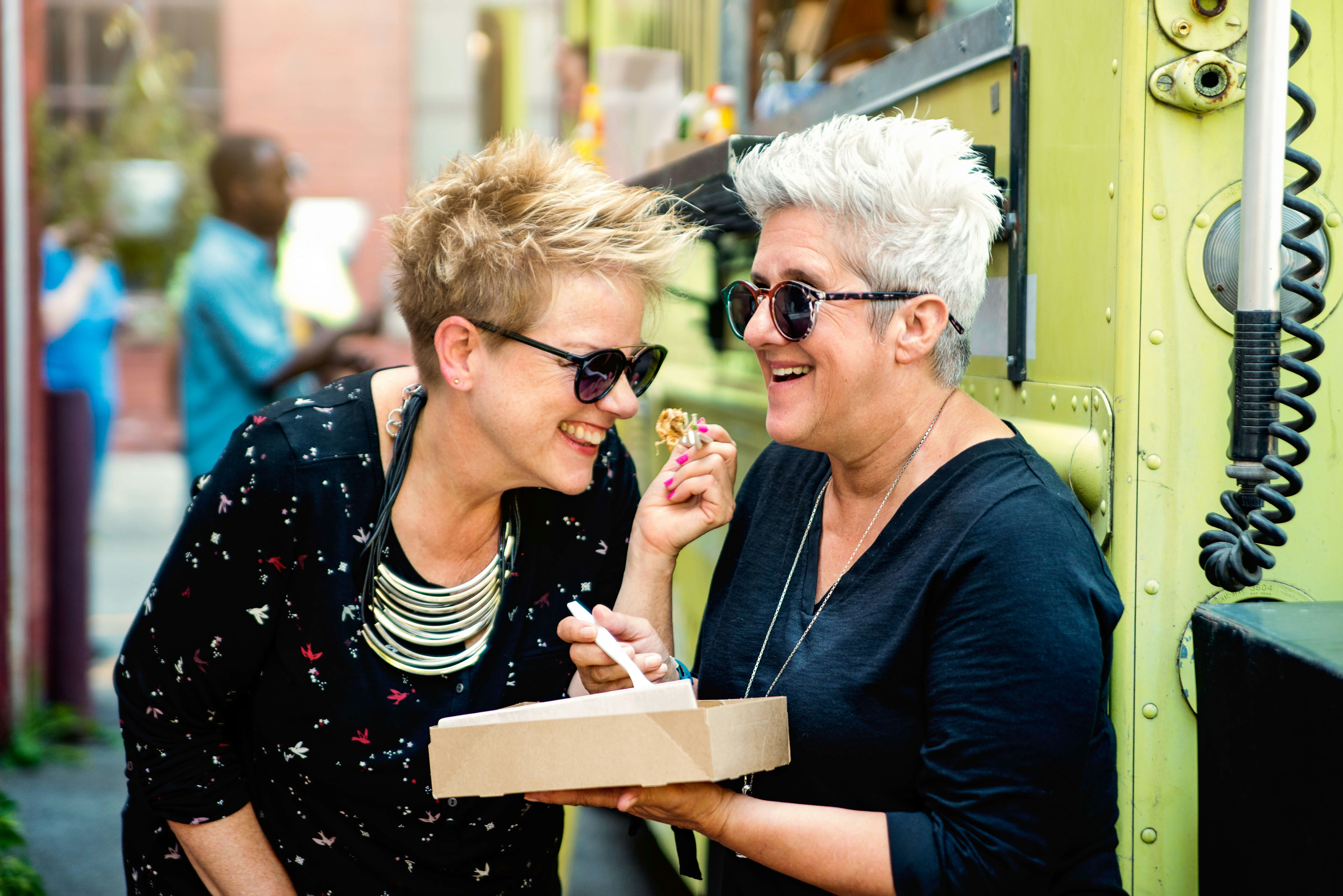 Couple of mature women enjoying their food from a food truck in city street.