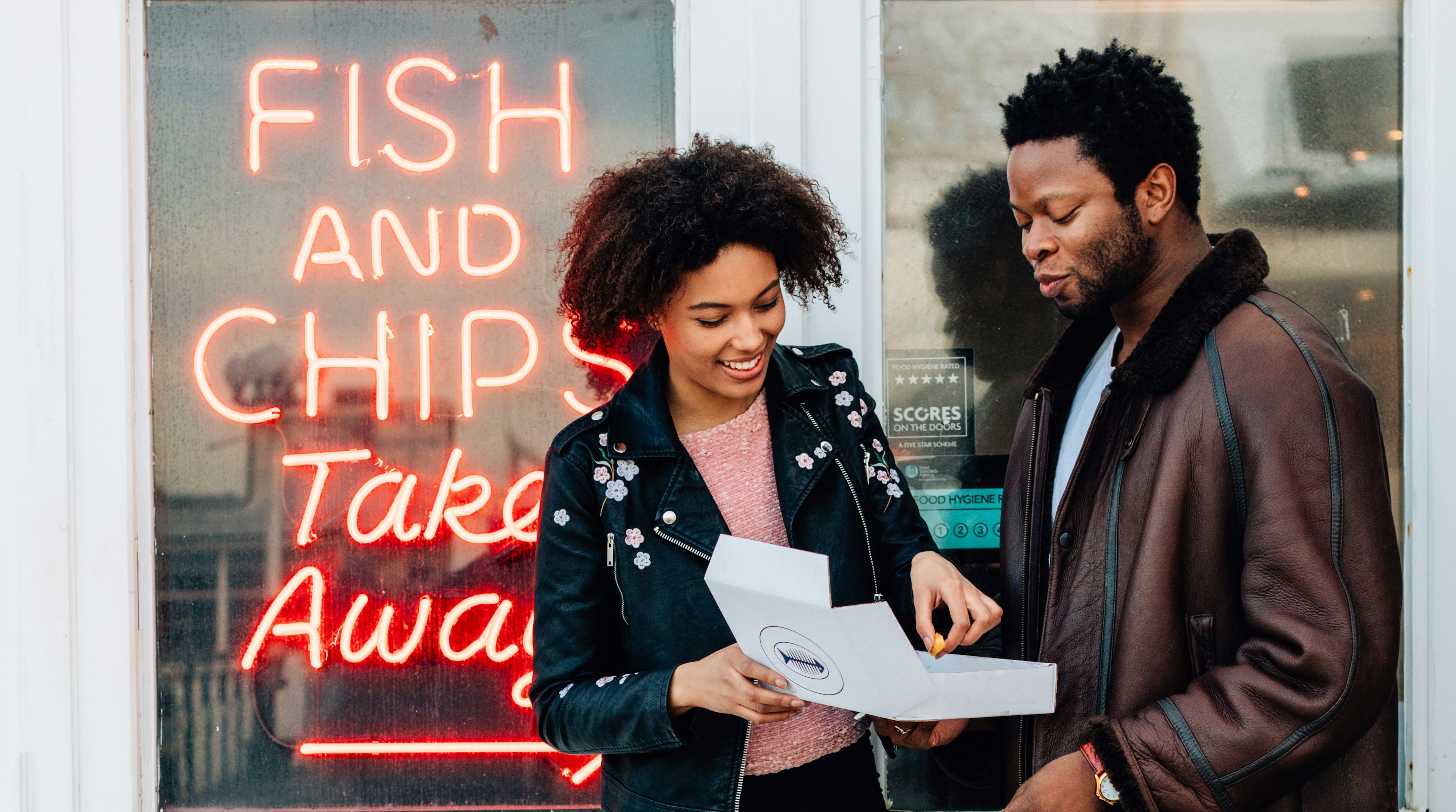 Couple enjoying fish and chips in Brighton by neon sign