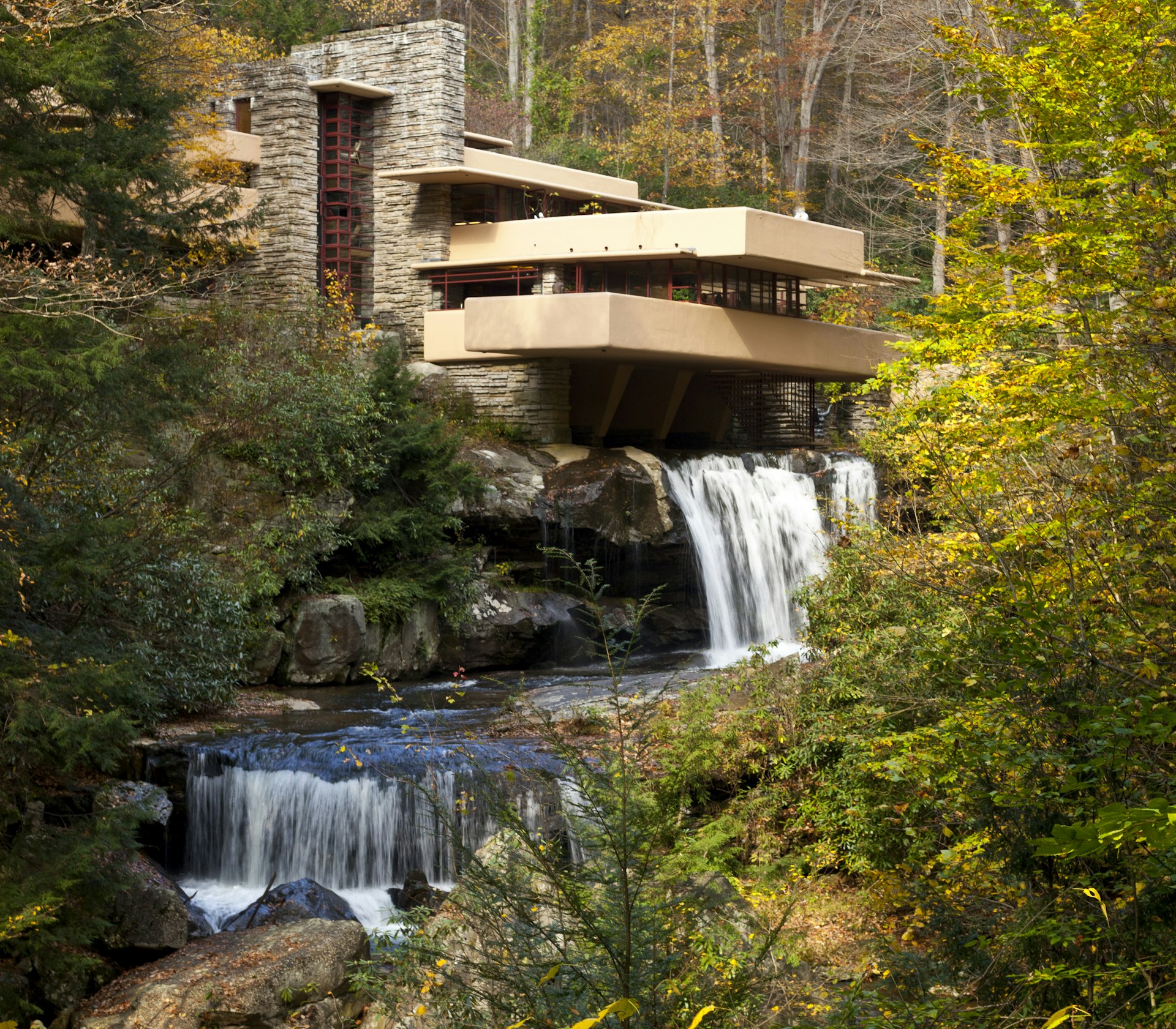Falling Water in Laurel Highlands is a Frank Lloyd Wright's masterpiece, within Bear Run Nature Reserve. There is a building overlooking a stream with two small waterfalls and flanked by tress and fallen leaves. 
