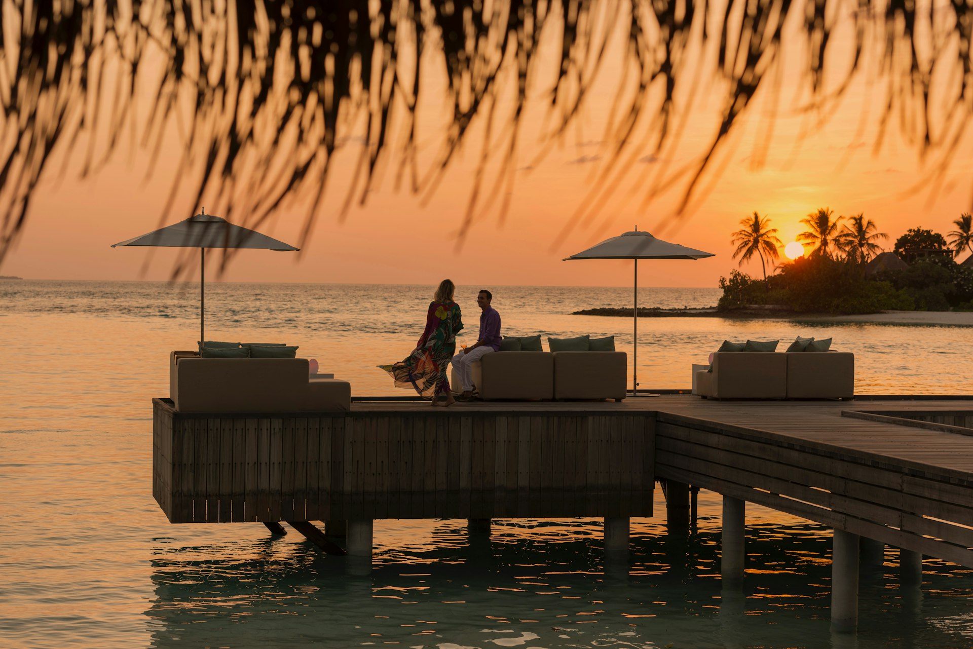 A couple on a dock watching a colorful sunset at Four Seasons Resort Maldives at Kuda Huraa