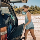 Young backpacker woman packing bags into the back of a 4x4 while on 75 Mile Beach on Fraser Island, Australia.