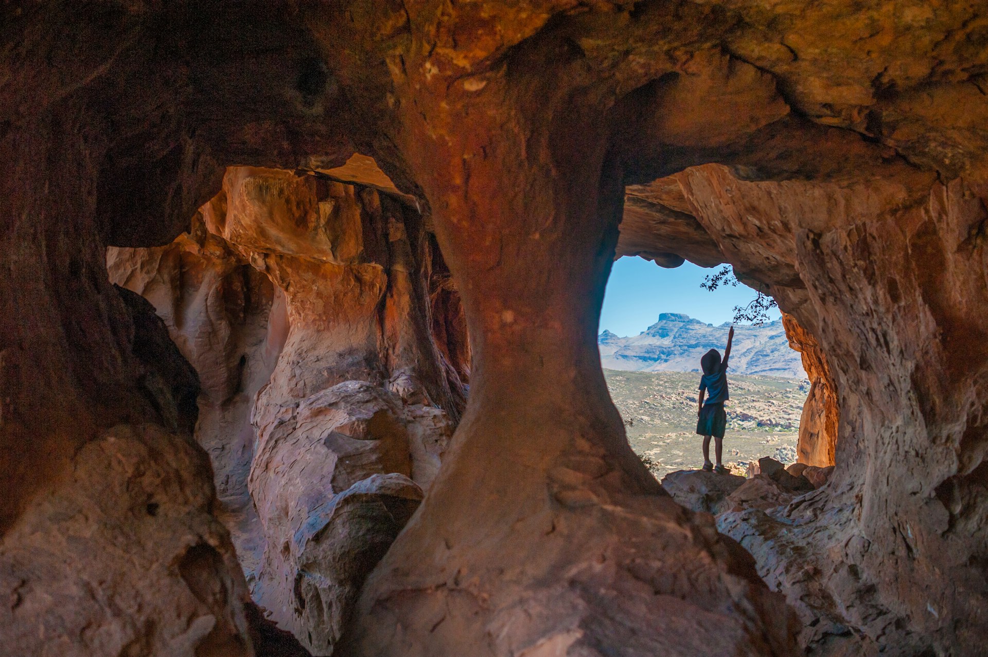 Young boy standing in a cave opening looking out onto the Cederberg Wilderness Area in South Africa