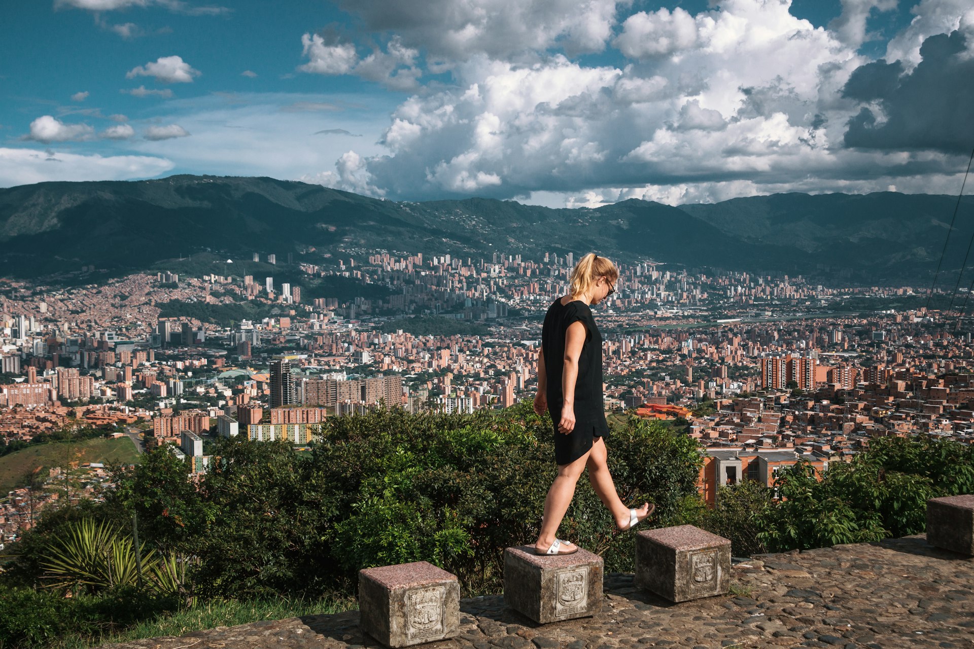A woman walks on stepping stones with a view of a city stretching out before her