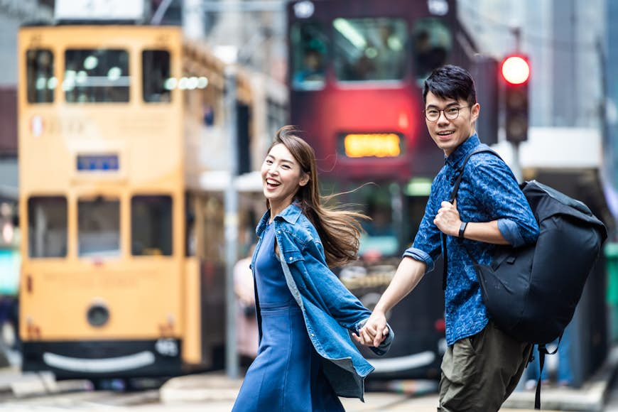 Two people walking in Hong Kong and holding hands in front of a bus and a tram