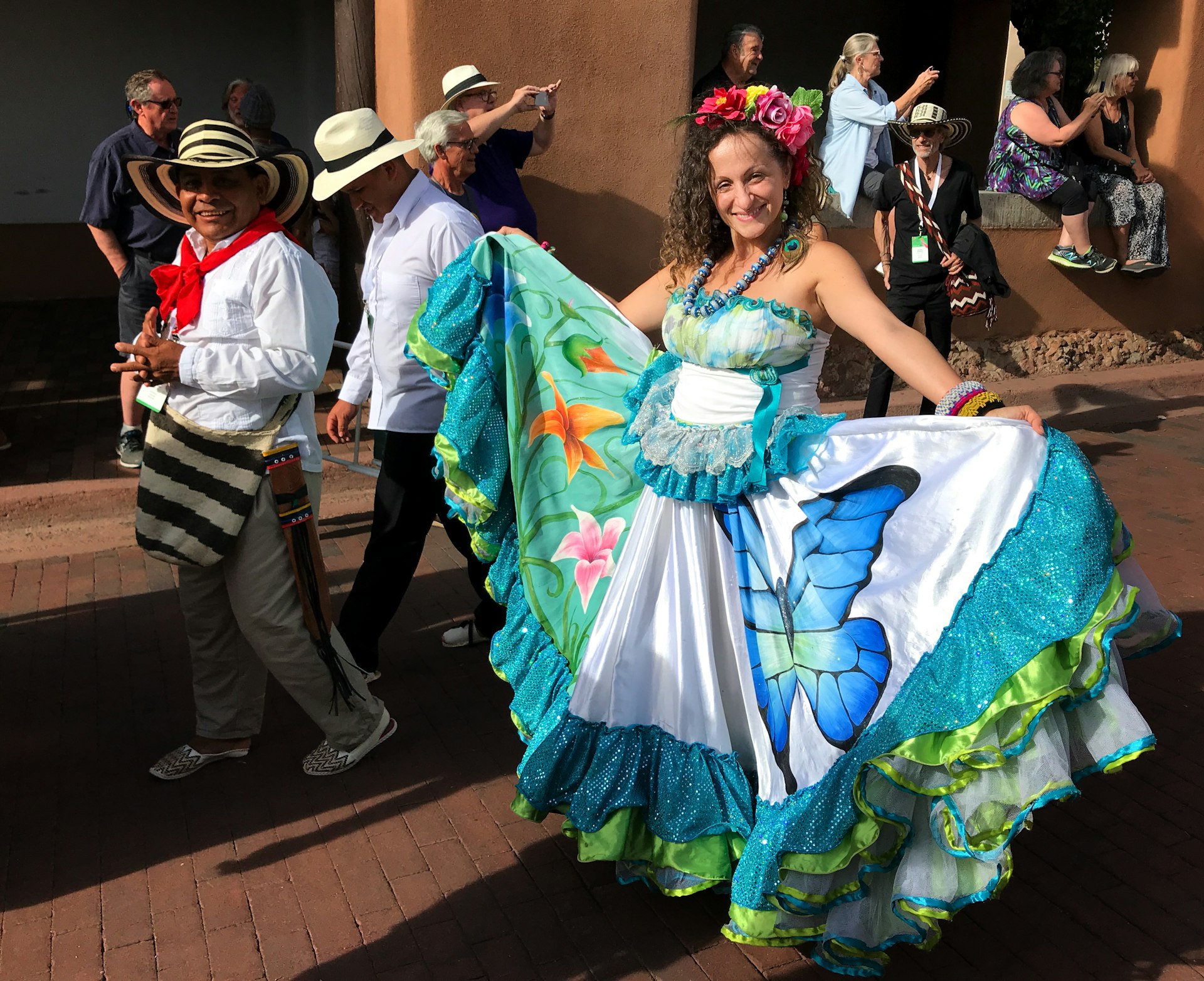 A woman smiles at the camera as she parades down a street. She's wearing a beautiful dress with intricate designs, which she proudly shows to the camera