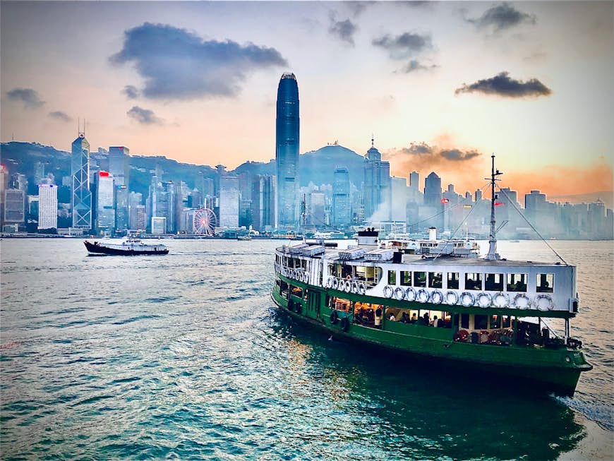The Star Ferry in Victoria Harbour, Hong Kong goes across the water towards skyscrapers at sunset