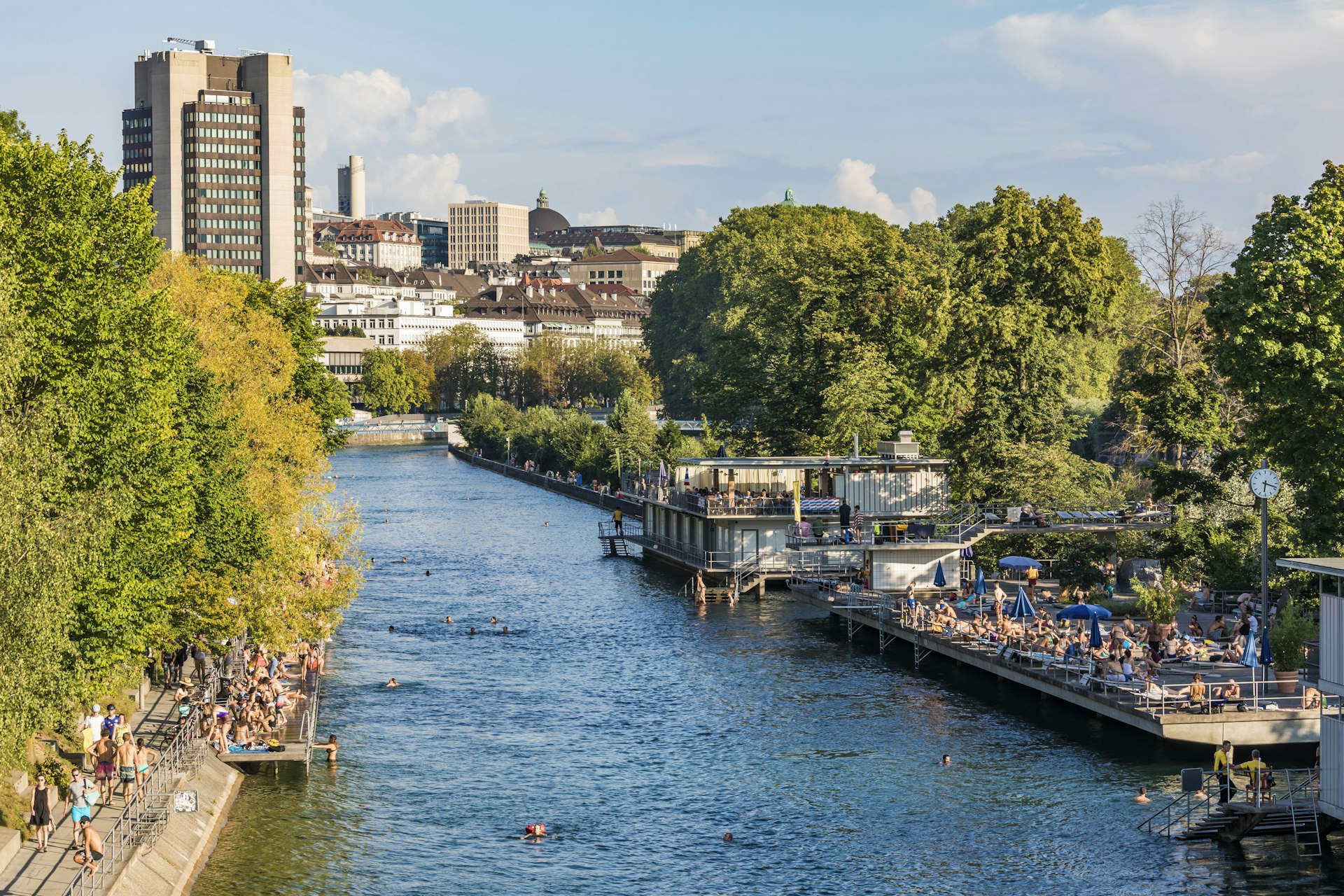People sunbathe on decking or swim in the river that runs through Zurich