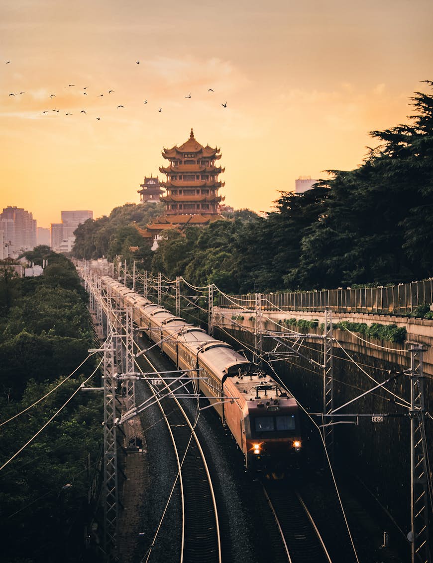 A train pulls out of Wuhan in China at sunrise with the pagoda-like Yellow Crane Tower in the background
