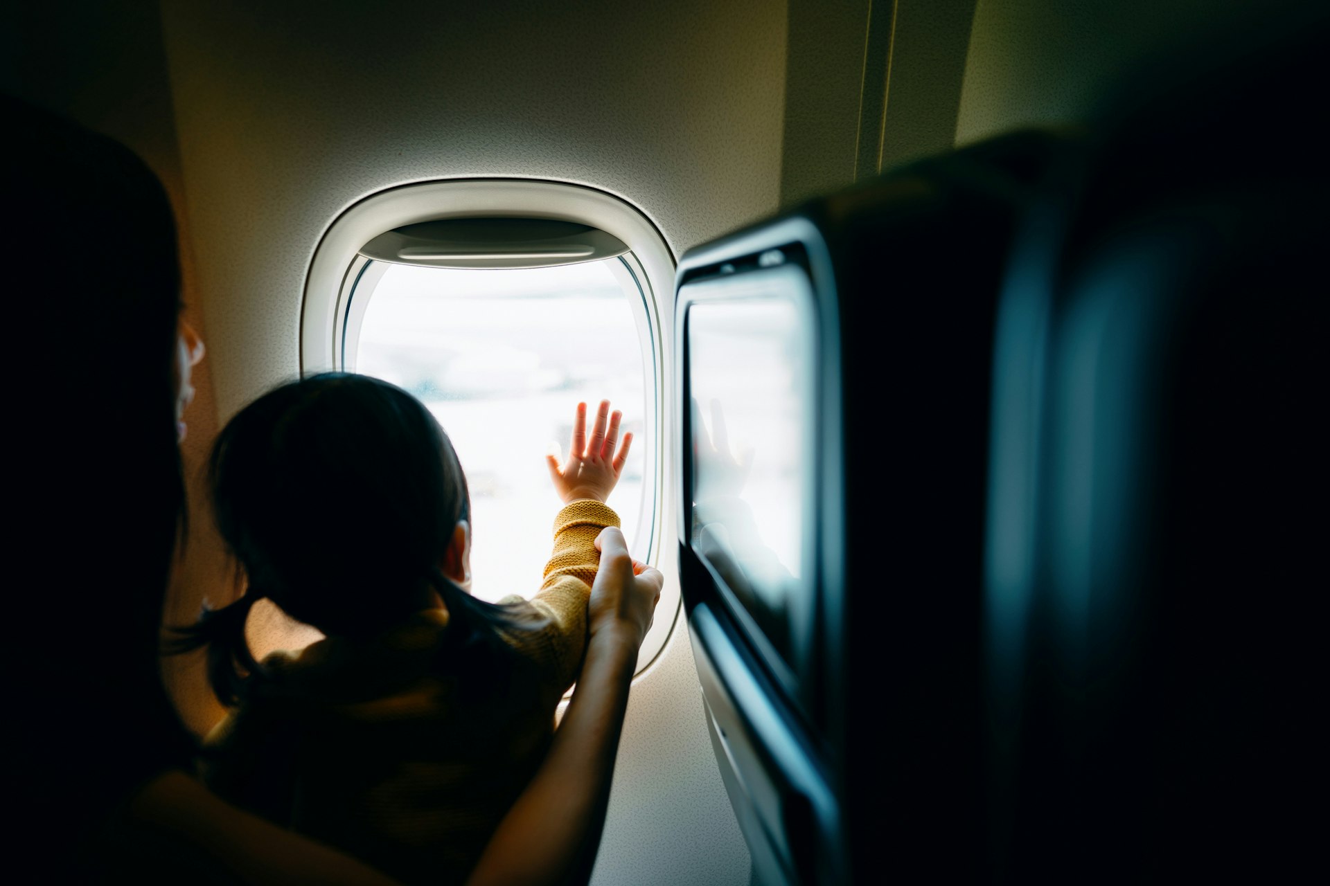 A young Asian mother and excited little daughter look out through an airplane window while travelling on holiday in Hong Kong