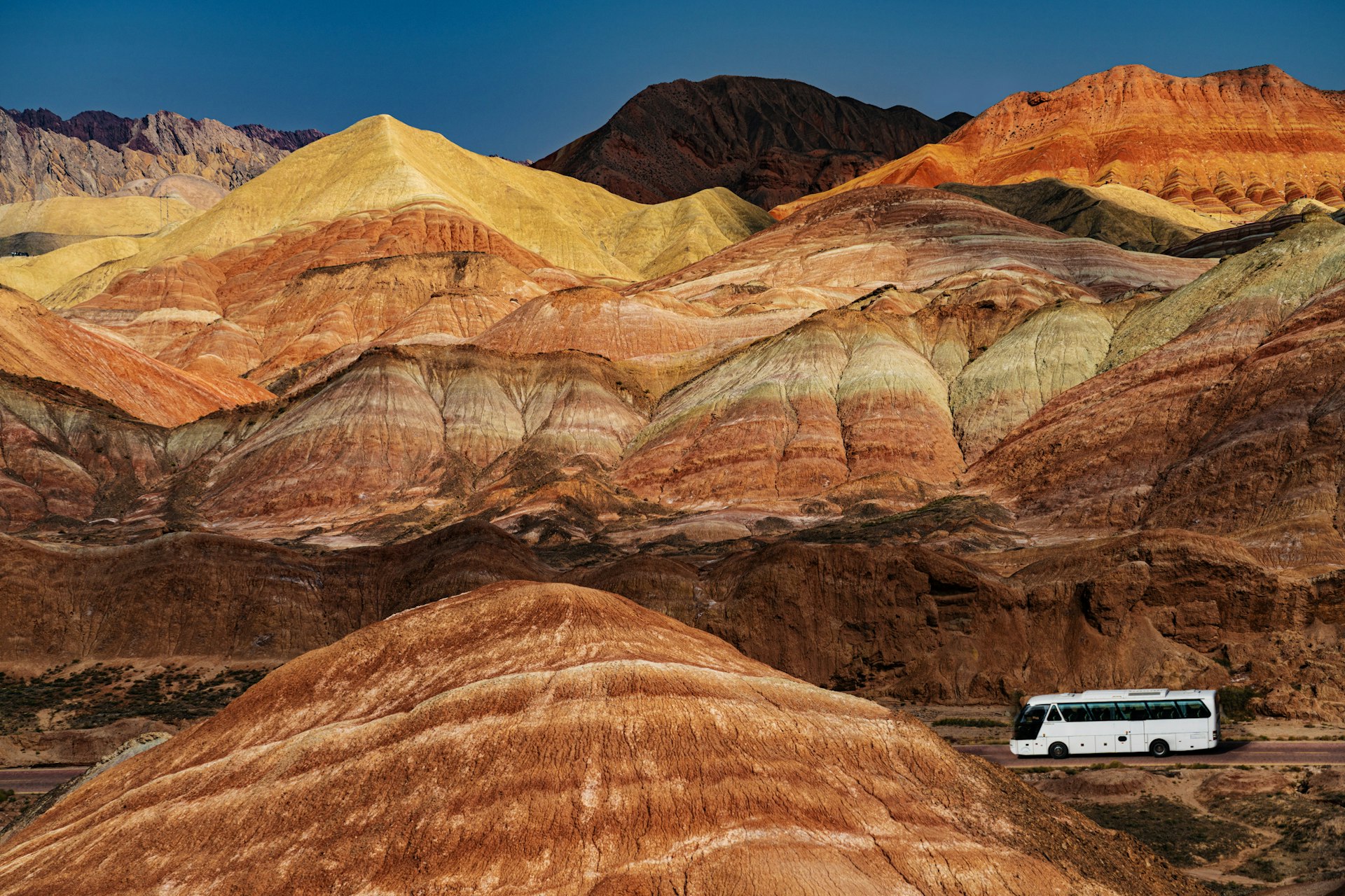 A white bus travels along the road in front of the brightly-coloured hills of Zhangye National Geopark in China