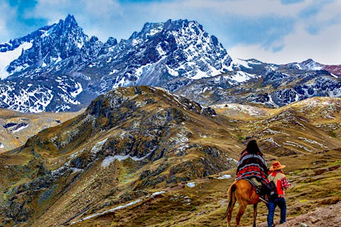 Woman on horseback and man walking beside through the Andes Mountains near Cusco, Peru 