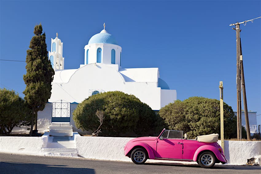 Ένα ροζ Volkswagen Beetle μπροστά από ένα παρεκκλήσι στη Σαντορίνη 