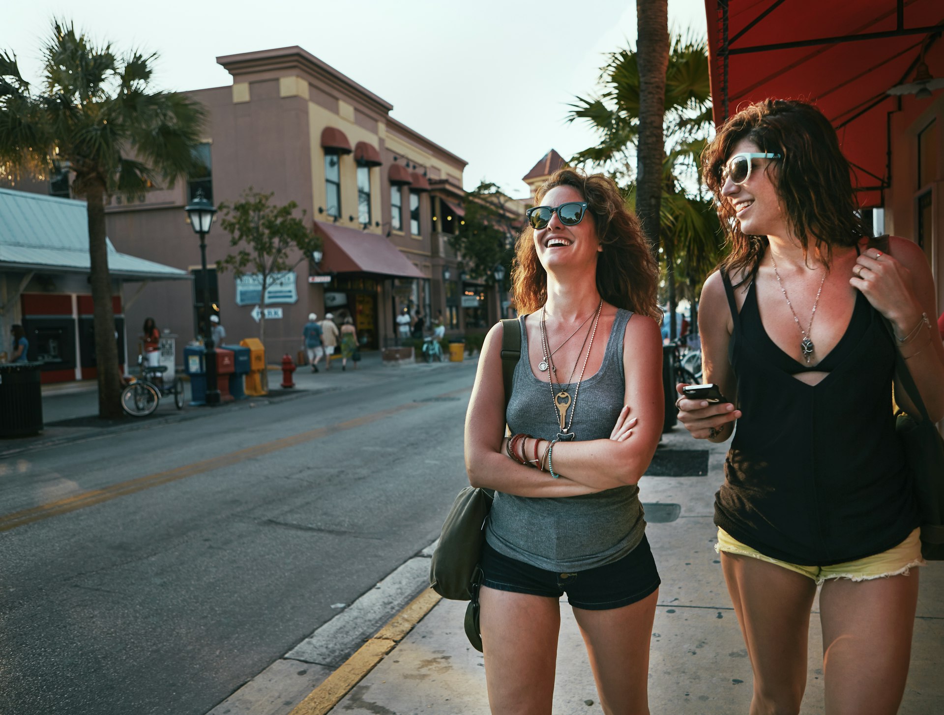 Two women laugh together while walking down a street in Key West