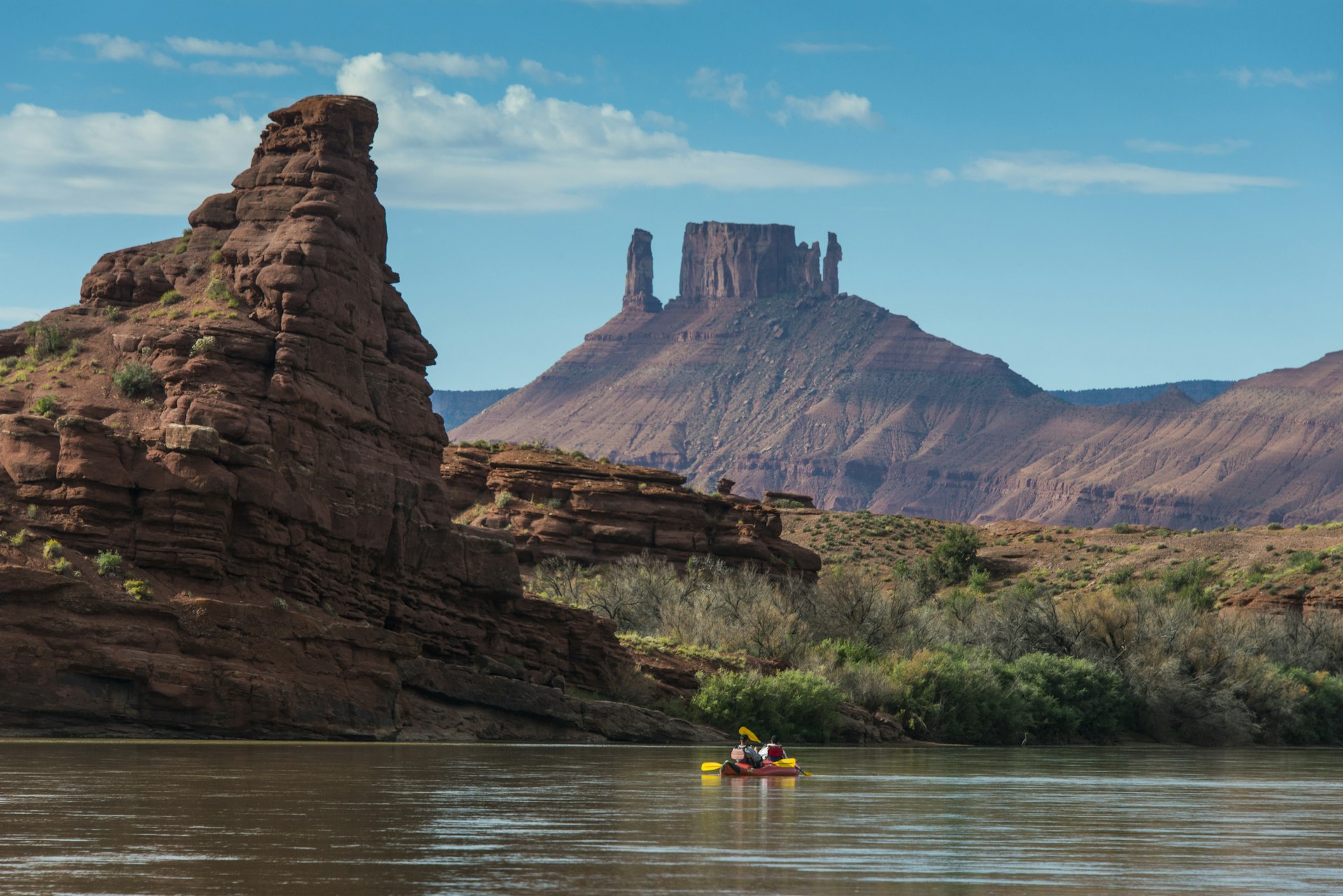 Couple kayaking down the Colorado River, with the large red rock formations of Castle Valley in the background.