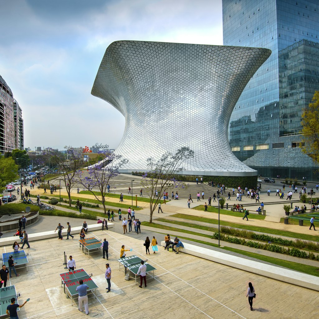 The aluminum-paneled Soumaya Museum stands in Plaza Carso in the Polanco district of Mexico City. The art museum/cultural institution has works from over 30 centuries of art. In the foreground workers on their lunch break enjoy a game of ping pong in the plaza.