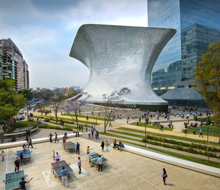 The aluminum-paneled Soumaya Museum stands in Plaza Carso in the Polanco district of Mexico City. The art museum/cultural institution has works from over 30 centuries of art. In the foreground workers on their lunch break enjoy a game of ping pong in the plaza.