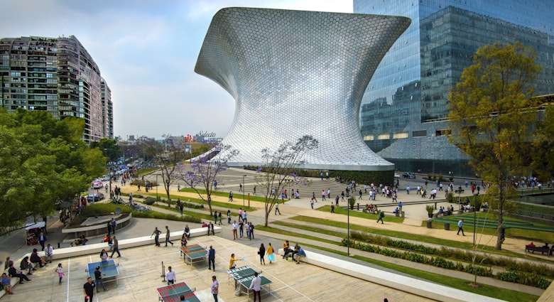 The aluminum-paneled Soumaya Museum stands in Plaza Carso in the Polanco district of Mexico City. The art museum/cultural institution has works from over 30 centuries of art. In the foreground workers on their lunch break enjoy a game of ping pong in the plaza.